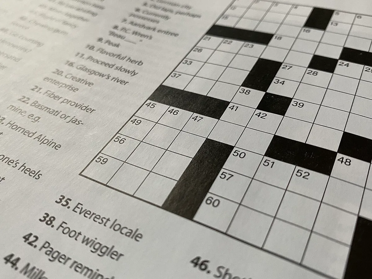 An empty crossword grid, seen at an angle, with numbered white squares, black blocks and a column of printed clues on the left.