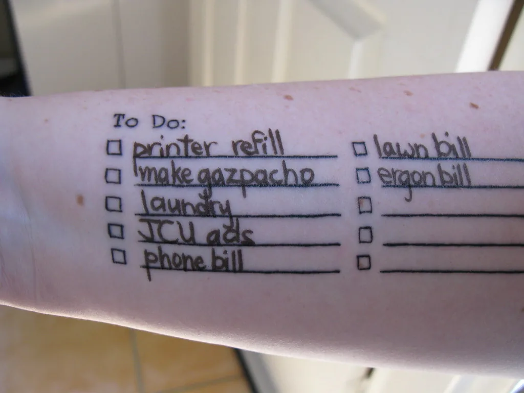 Un avant-bras sur lequel une liste de choses à faire est dessinée à même la peau : recharge d’imprimante, gaspacho, lessive, facture de téléphone, chacune avec sa case à cocher, et quelques lignes encore vides.