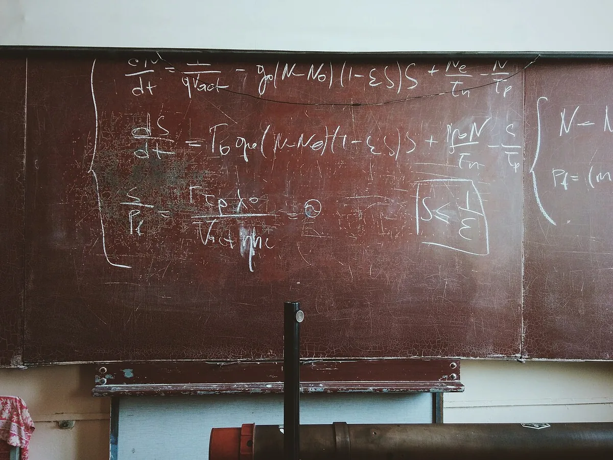 Close-up of a worn chalkboard filled with handwritten differential equations, a curly bracket on the left and a short inequality boxed on the right.